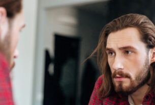 Homem em dúvida olhando para si mesmo no espelho, representando insegurança e conflitos no universo cuckold, se achando um falso cuckold.