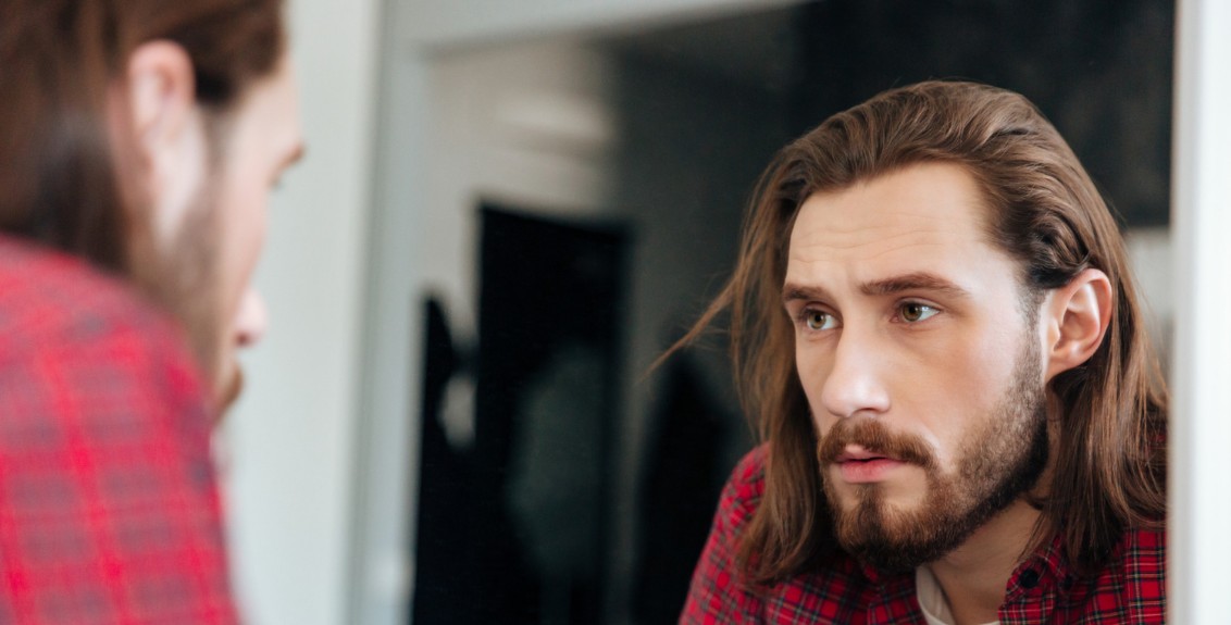 Homem em dúvida olhando para si mesmo no espelho, representando insegurança e conflitos no universo cuckold, se achando um falso cuckold.